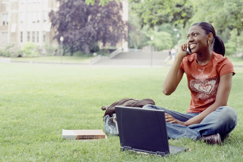 Young female student using mobile phone on university lawn